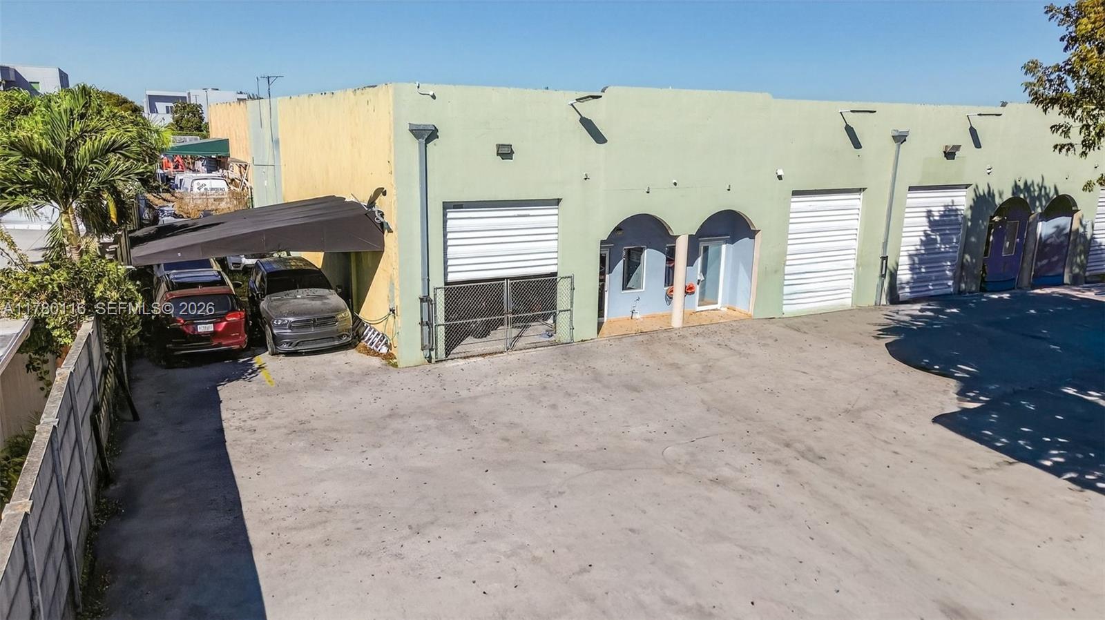 An exterior view of a light green commercial building with multiple roll-up garage doors — 9180 NW 119th St # 10, Hialeah Gardens FL 33018, HIALEAH GARDENS, FL