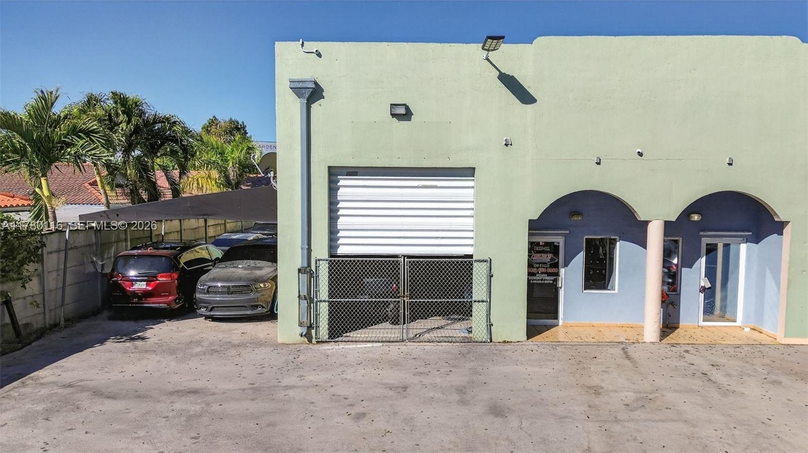 A light green commercial building features a roll-up garage door and an arched entryway — 9180 NW 119th St # 10, Hialeah Gardens FL 33018, HIALEAH GARDENS, FL