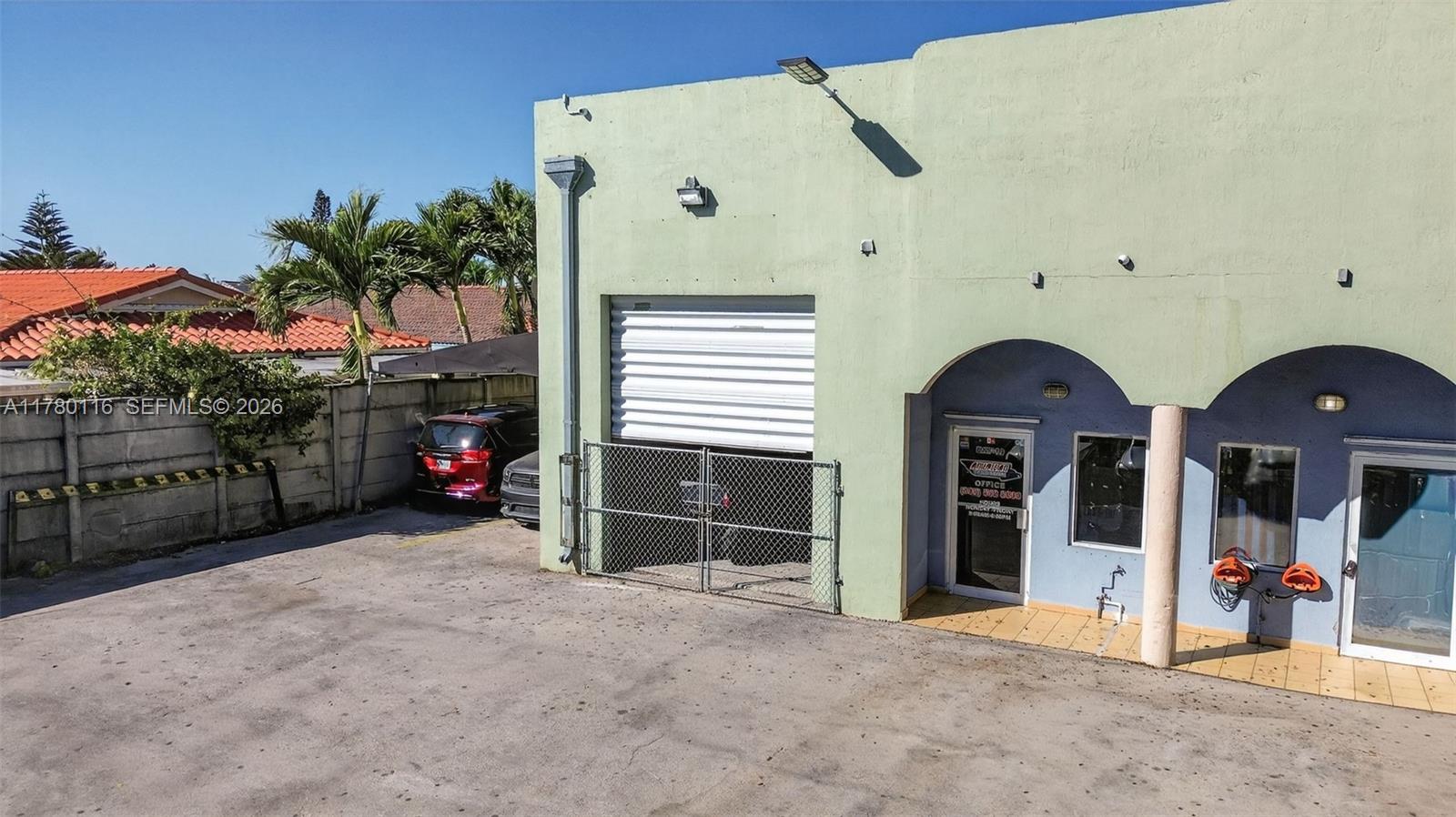 An exterior view of a light green commercial building with a roll-up door and arched entrances — 9180 NW 119th St # 10, Hialeah Gardens FL 33018, HIALEAH GARDENS, FL
