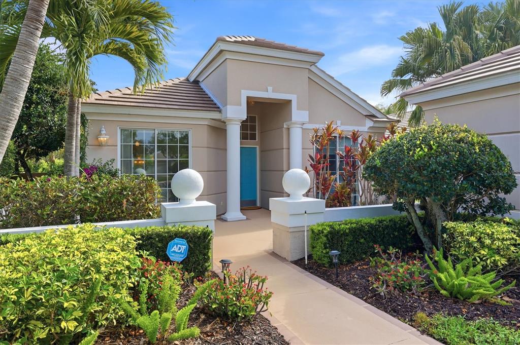 A beige single-story house features a blue front door, white columns, and a landscaped walkway — 7119 KENSINGTON COURT, UNIVERSITY PARK, FL