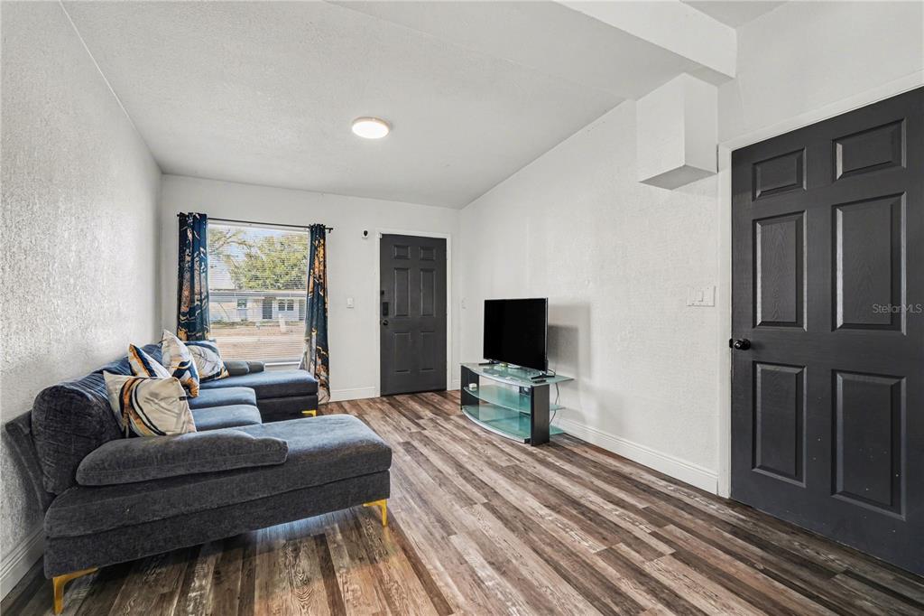 A living room features a gray sectional sofa, a television on a glass stand, and wood-look flooring — 4928 S 82ND STREET, TAMPA, FL
