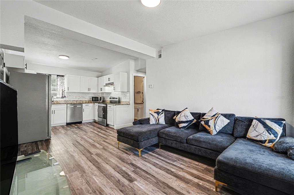 An open-concept living room with wood-look flooring flows into a kitchen with white cabinets — 4928 S 82ND STREET, TAMPA, FL