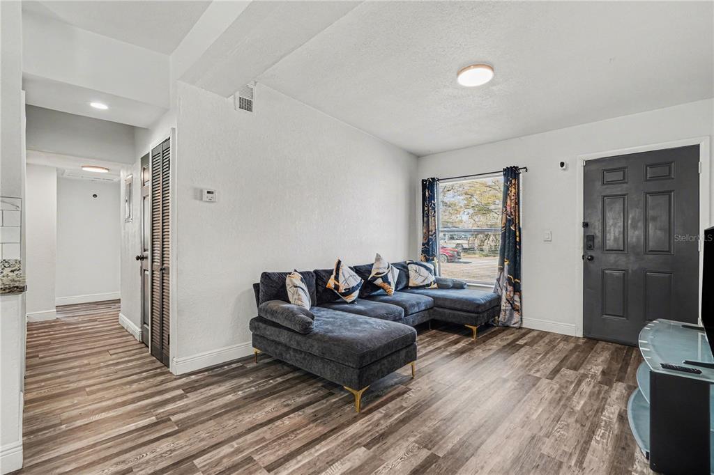 A living room features a dark gray sectional sofa, wood-look flooring, and a front door — 4928 S 82ND STREET, TAMPA, FL
