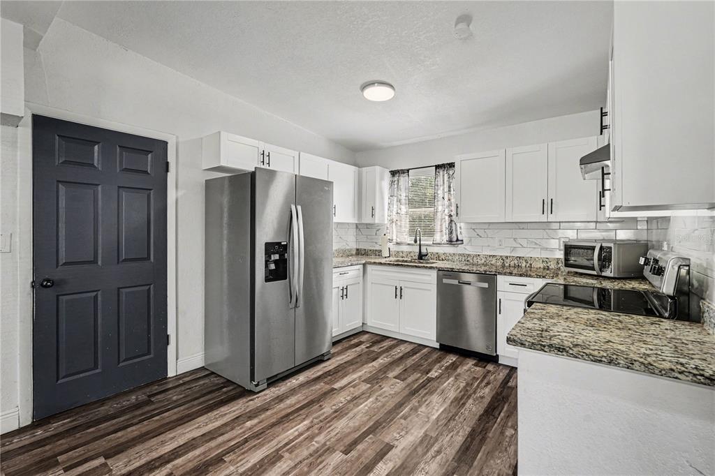 A kitchen features white cabinets, stainless steel appliances, granite countertops, and wood-look flooring — 4928 S 82ND STREET, TAMPA, FL