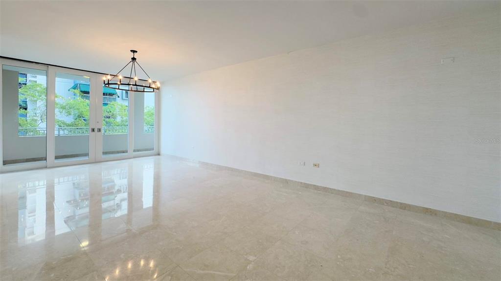 An empty room features light-colored tile flooring, white walls, and a modern chandelier — 1-02 CAOBA STREET UNIT 312-6, GUAYNABO, PR