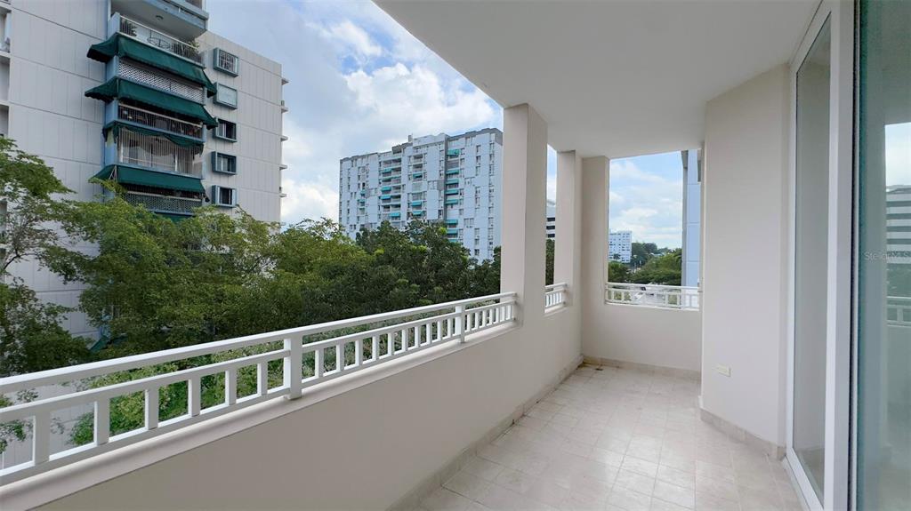 A white tiled balcony features a metal railing overlooking trees and nearby apartment buildings — 1-02 CAOBA STREET UNIT 312-6, GUAYNABO, PR