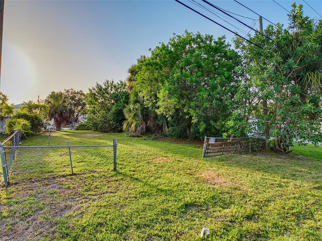 A grassy, fenced-in vacant lot features several mature trees and shrubs under a clear sky — 14905 OLD DIXIE HIGHWAY, HUDSON, FL