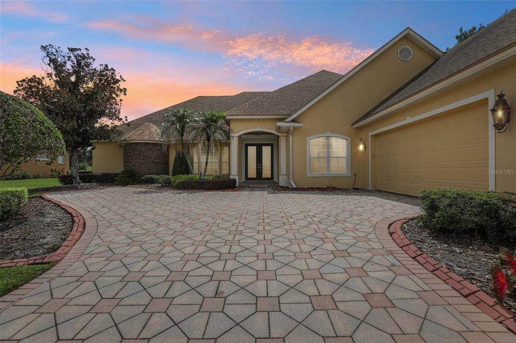 A single-story house with a paved driveway, tan stucco exterior, and a two-car garage — 7360 REFLECTIONS LAKE DRIVE, LAKELAND, FL