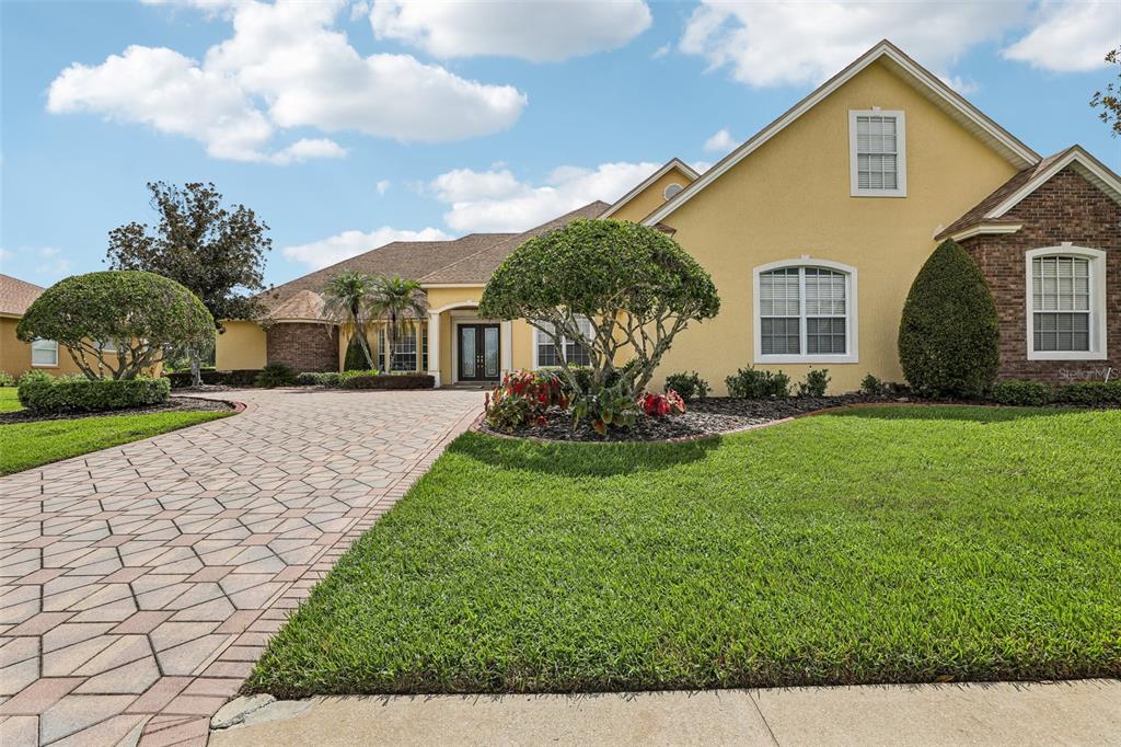 A single-story house with a yellow stucco exterior, brick accents, and a paved driveway — 7360 REFLECTIONS LAKE DRIVE, LAKELAND, FL
