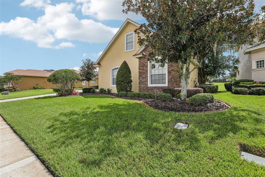 A yellow house with a brick accent wall and a manicured lawn under a blue sky — 7360 REFLECTIONS LAKE DRIVE, LAKELAND, FL