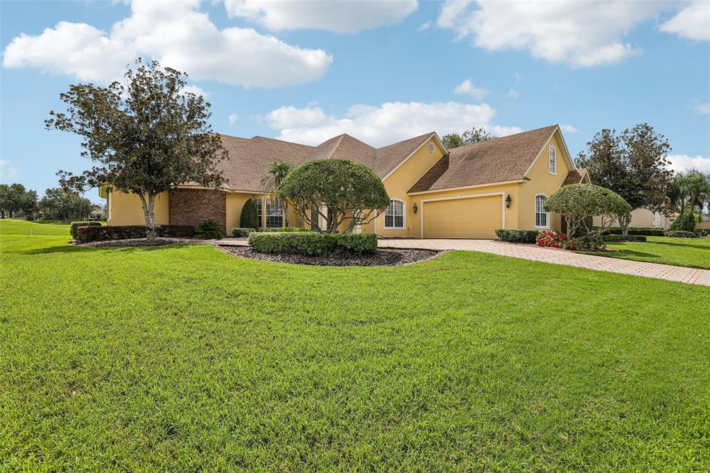 A yellow single-story house with a brick accent wall, a paved driveway, and manicured landscaping — 7360 REFLECTIONS LAKE DRIVE, LAKELAND, FL