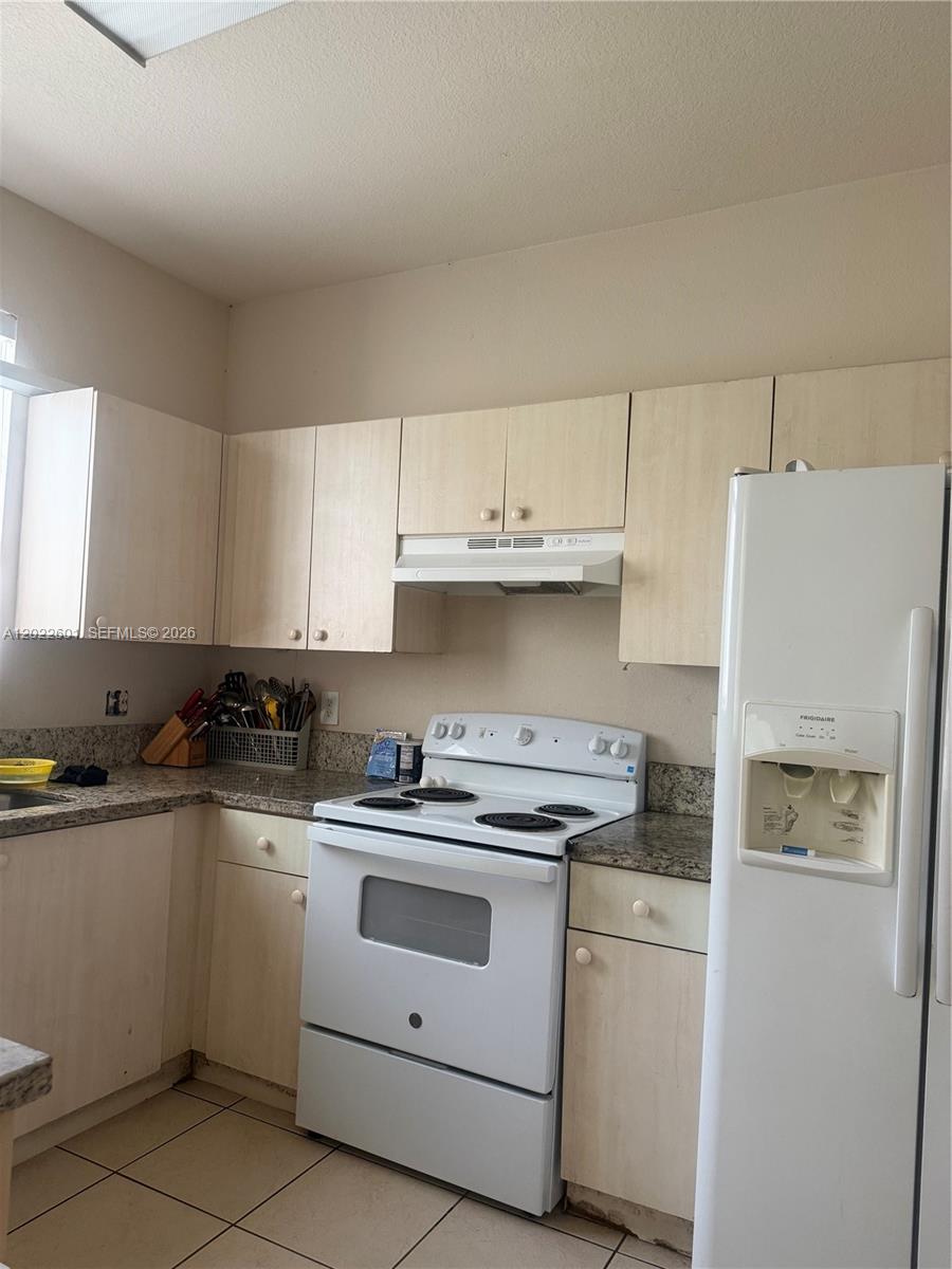 A kitchen features light wood cabinets, granite countertops, white appliances, and tiled flooring — 101 SW 15th Rd # 101, Homestead FL 33030, HOMESTEAD, FL