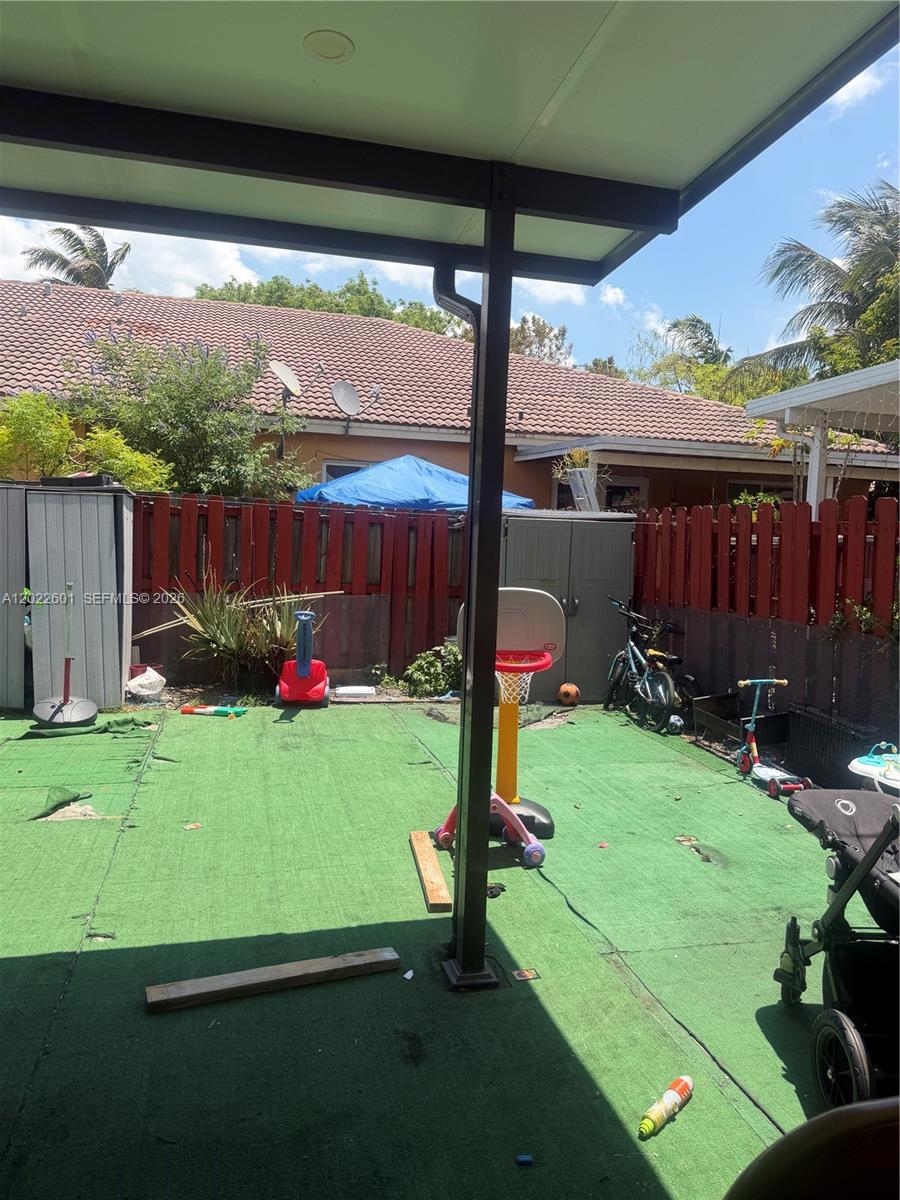 A backyard patio features artificial turf, a basketball hoop, and a red wooden fence — 101 SW 15th Rd # 101, Homestead FL 33030, HOMESTEAD, FL