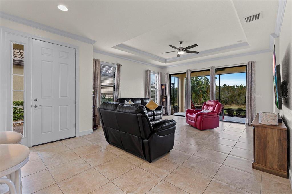 A living room with tile floors, a tray ceiling, a black sofa, and a red chair — 8424 ALBERATA VISTA DRIVE, TAMPA, FL