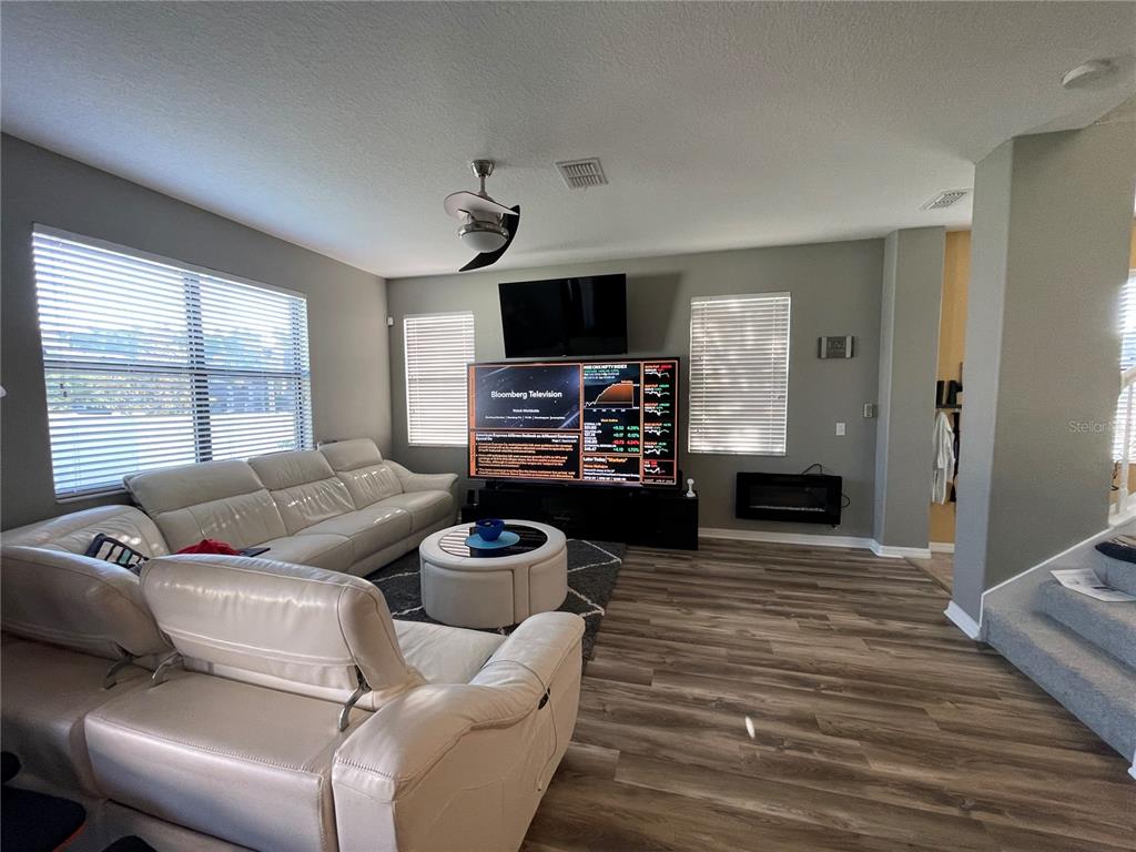 A living room features light wood-look flooring, a white sectional sofa, and a wall-mounted television — 11796 CRESTRIDGE LOOP, NEW PORT RICHEY, FL