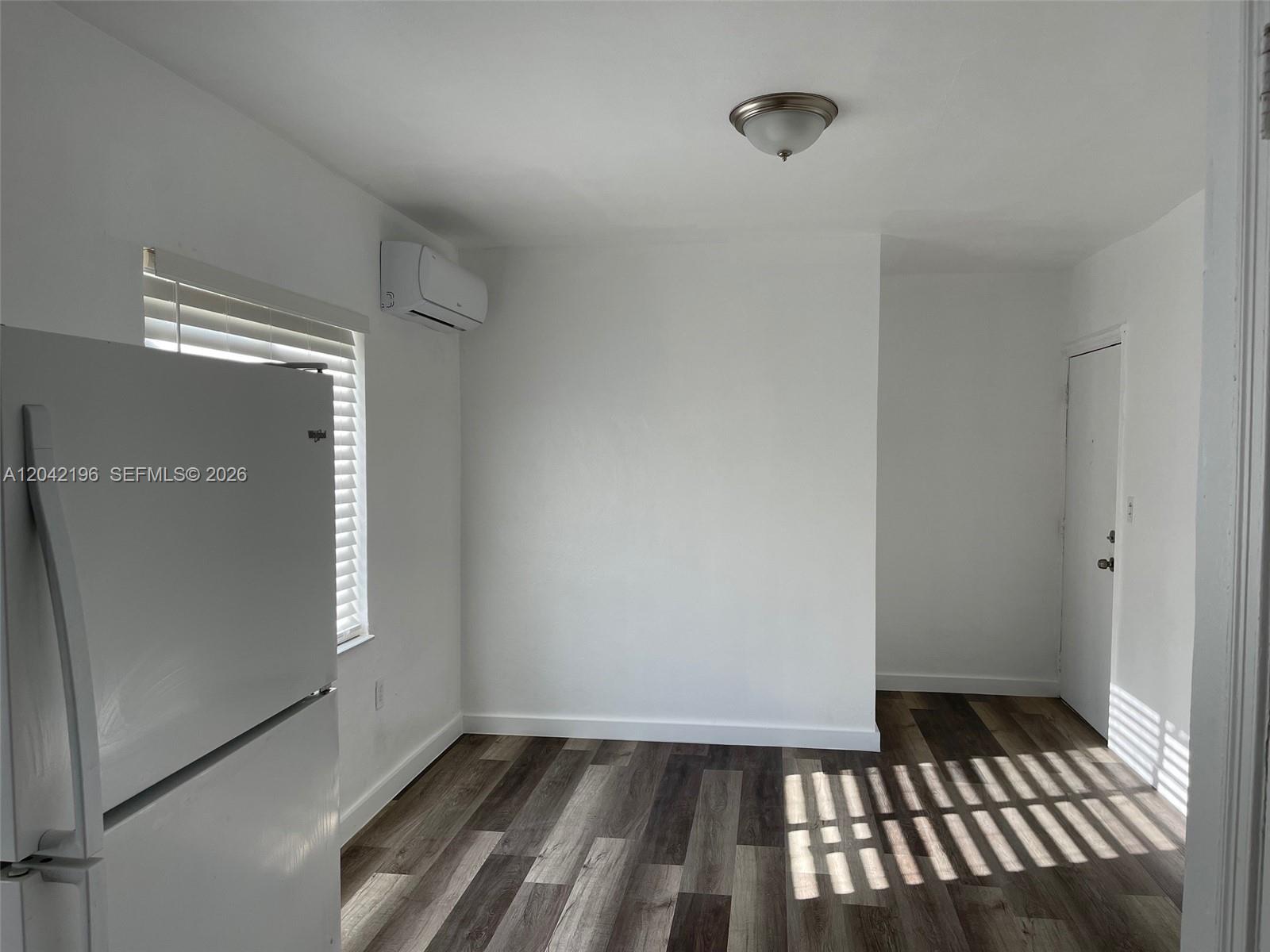 A room with white walls, wood-look flooring, a refrigerator, and a wall-mounted air conditioner — 430 SW 6th Ave # 8, Miami FL 33130, MIAMI, FL