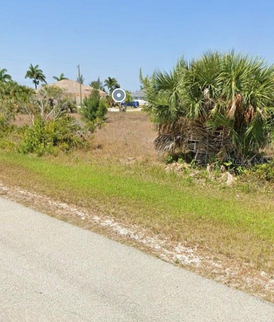A vacant, grassy lot with scattered palm trees and shrubs sits beside a paved road — 15835 MELPORT CIRCLE, PORT CHARLOTTE, FL