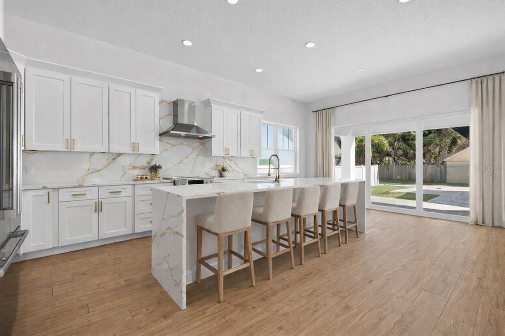 A modern kitchen features white cabinetry, gold hardware, a marble-patterned island, and sliding glass doors — 842 30TH AVENUE, ST PETERSBURG, FL