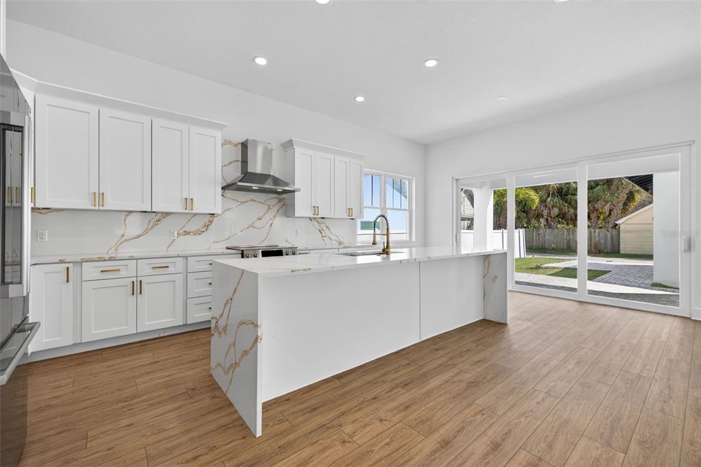 A bright kitchen features white cabinets, marble-patterned countertops, a large island, and sliding glass doors — 842 30TH AVENUE, ST PETERSBURG, FL