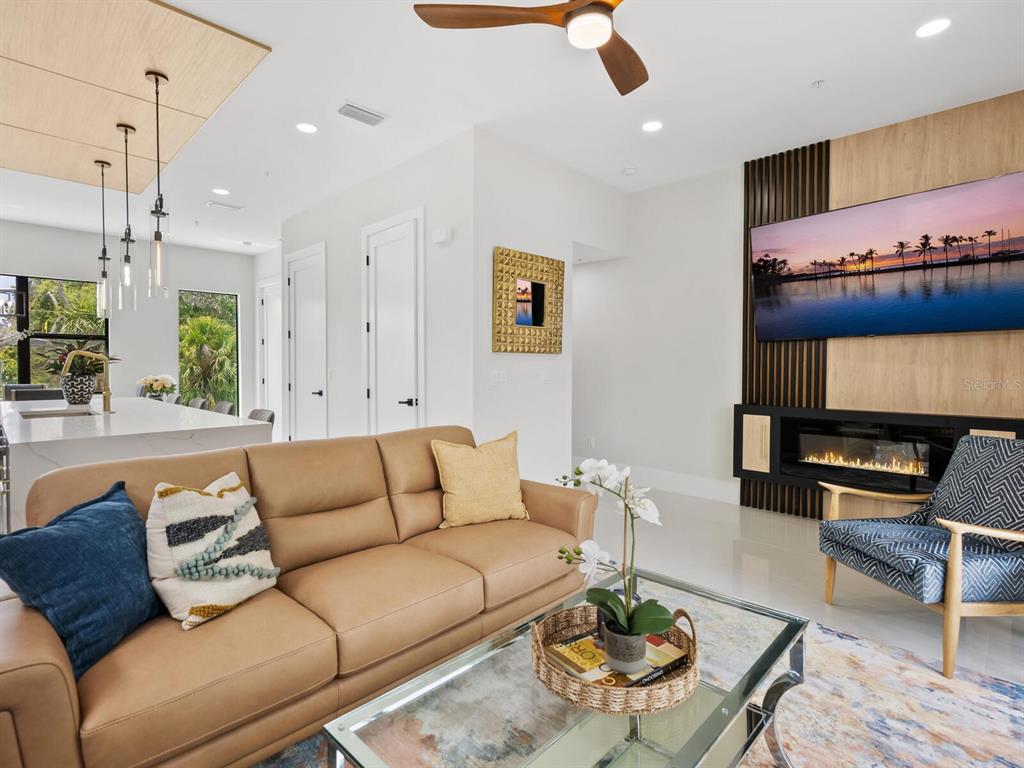 A modern living room features a tan leather sofa, glass coffee table, and a fireplace wall — 152 AUDUBON PLACE, SARASOTA, FL