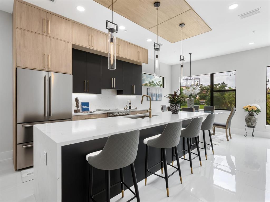 A modern kitchen features a white quartz island, two-tone cabinetry, and three hanging pendant lights — 152 AUDUBON PLACE, SARASOTA, FL