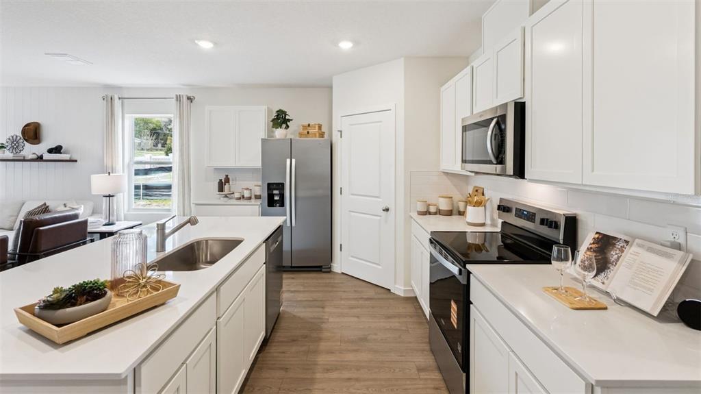 A modern kitchen features white cabinets, stainless steel appliances, and a large center island — 4919 MARSHELDER STREET, APOPKA, FL