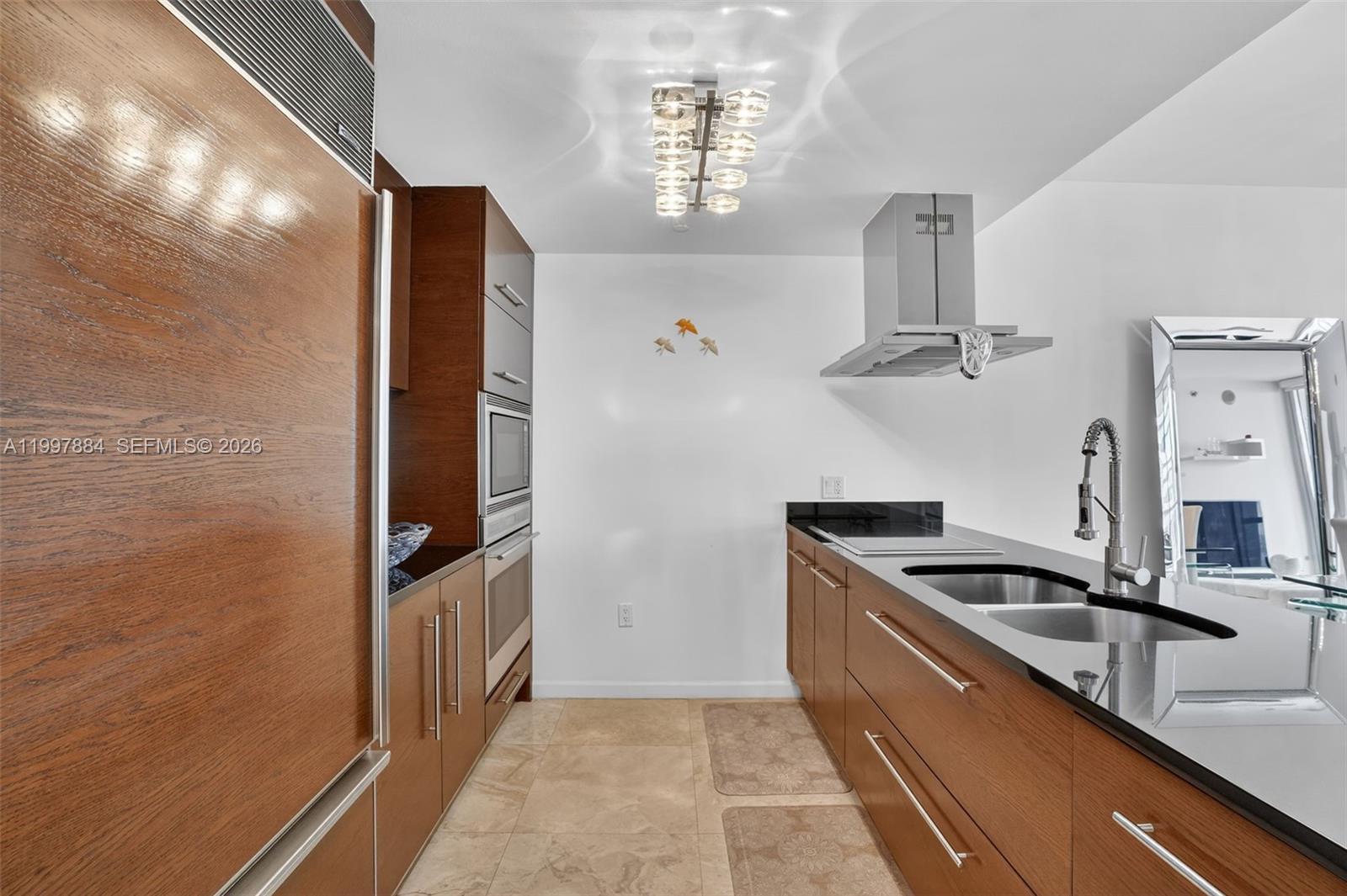A galley kitchen features wood cabinetry, black countertops, stainless steel appliances, and tile flooring — 495 Brickell Ave # 2807, Miami FL 33131, MIAMI, FL