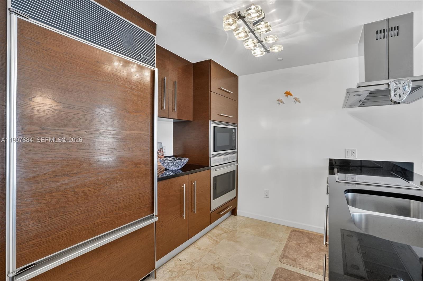A kitchen features wood-paneled cabinetry, stainless steel appliances, black countertops, and tile flooring — 495 Brickell Ave # 2807, Miami FL 33131, MIAMI, FL
