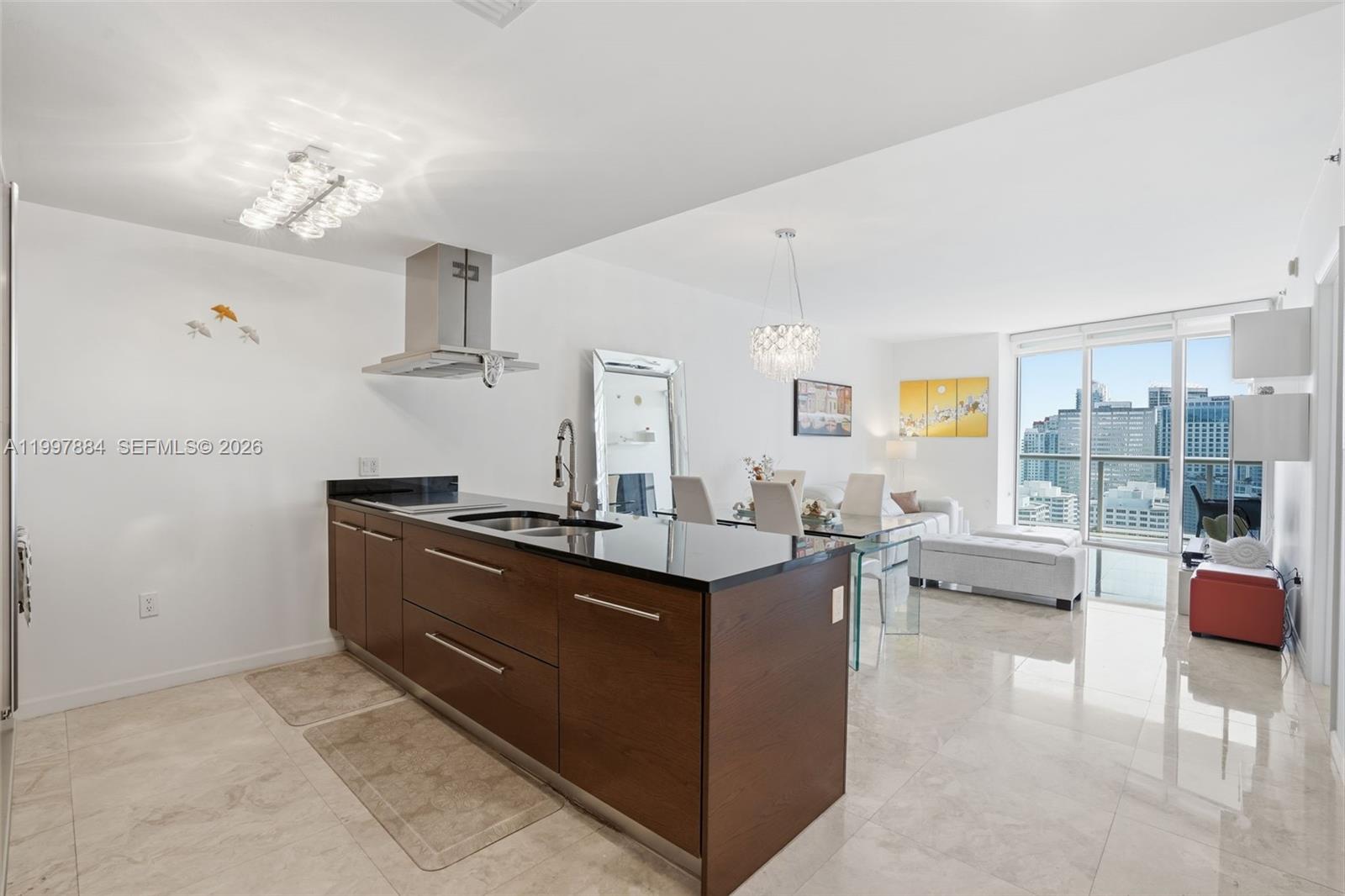 A modern kitchen with dark wood cabinets and black countertops opens into a bright living area — 495 Brickell Ave # 2807, Miami FL 33131, MIAMI, FL