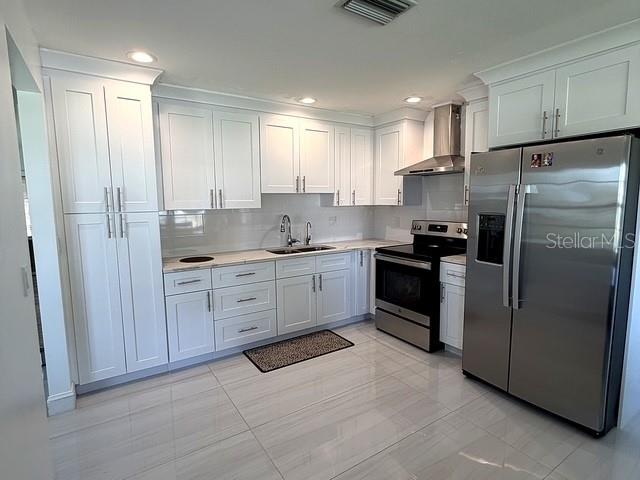 A modern kitchen features white cabinetry, stainless steel appliances, and light-colored tile flooring — 1629 WILLOW RUN, SEBRING, FL