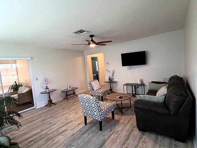 A living room features light wood-look flooring, a dark sofa, and a patterned accent chair — 1629 WILLOW RUN, SEBRING, FL