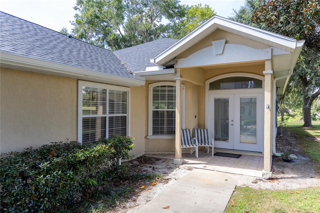 A beige house exterior features a covered entryway with double glass doors and two chairs — 6494 NW 109TH PLACE, ALACHUA, FL