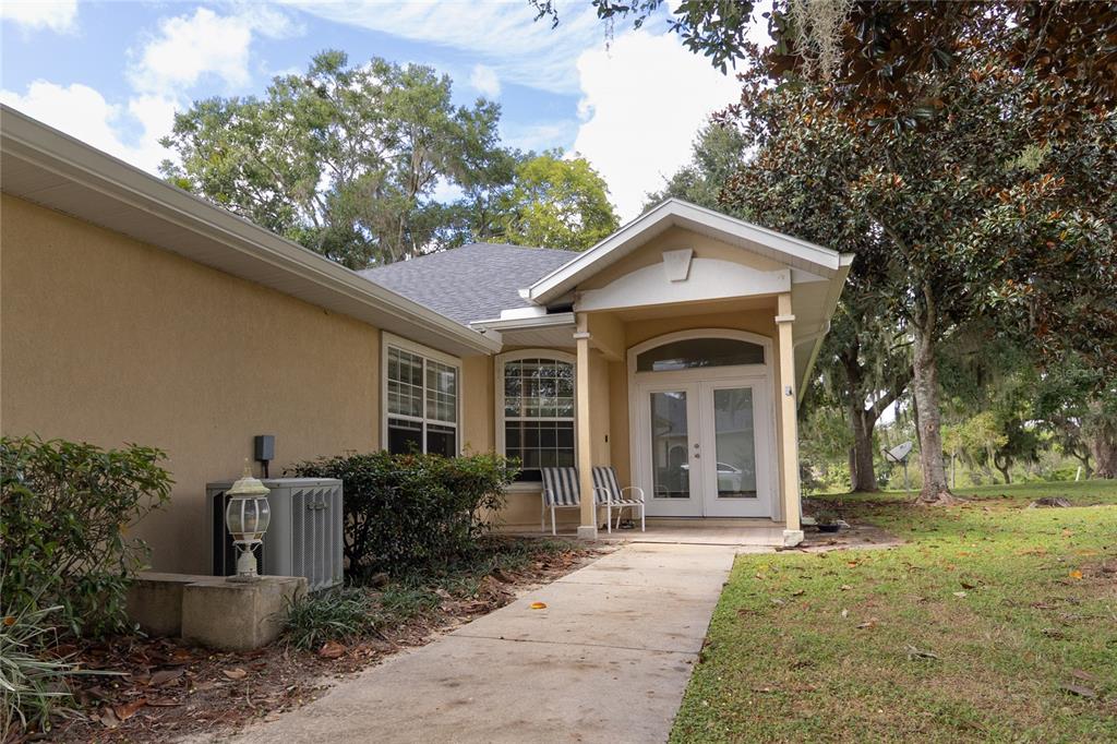 A concrete walkway leads to the covered front entrance of a tan stucco house — 6494 NW 109TH PLACE, ALACHUA, FL