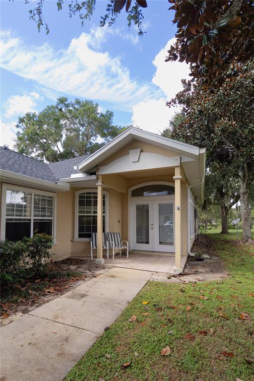 A tan house exterior features a covered entryway with double glass doors and a concrete walkway — 6494 NW 109TH PLACE, ALACHUA, FL