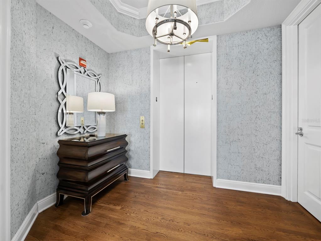 An entryway features a private elevator, textured gray wallpaper, a dark wood chest, and mirror — 35 WATERGATE DRIVE UNIT 1403, SARASOTA, FL