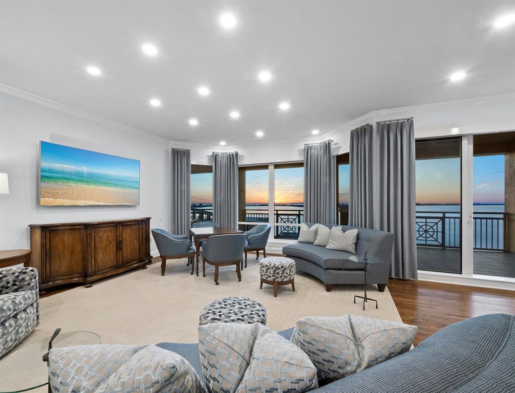 A living room features blue furniture, a large television, and floor-to-ceiling windows overlooking the water — 35 WATERGATE DRIVE UNIT 1403, SARASOTA, FL