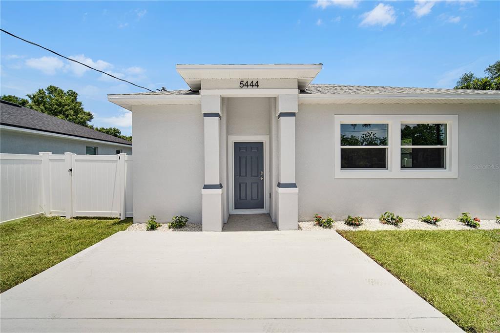A light-colored house exterior features a gray front door, concrete driveway, and white fencing — 5444 SIMMONS RD, LAKELAND, FL