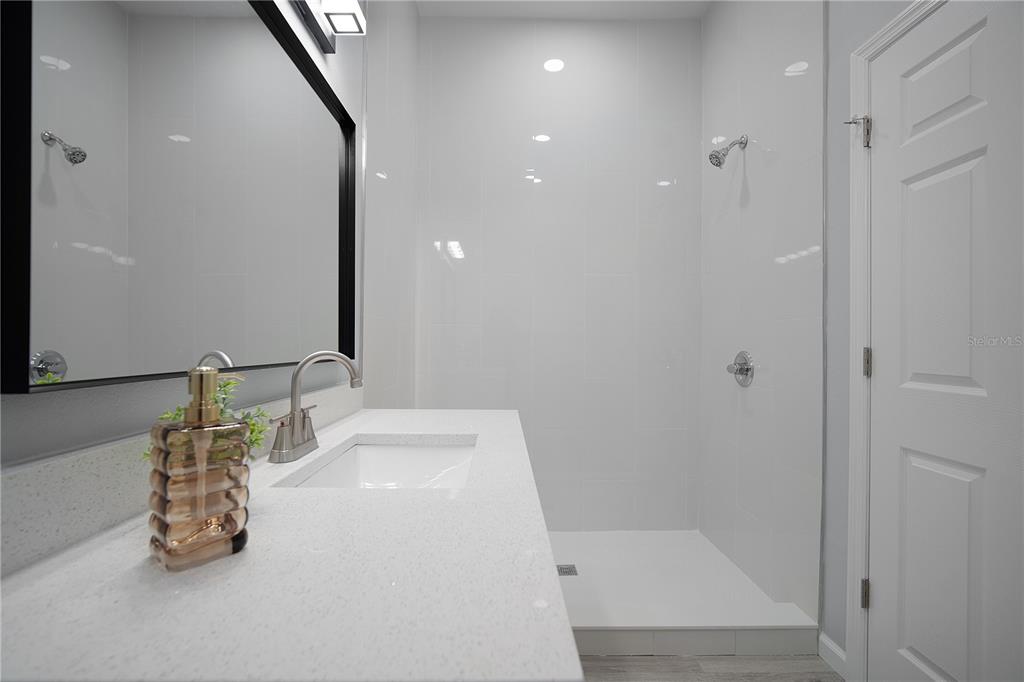 A modern bathroom features a white quartz vanity, a black-framed mirror, and a tiled shower — 5444 SIMMONS RD, LAKELAND, FL