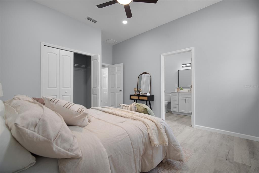 A bedroom with light gray walls, wood-look flooring, a ceiling fan, and an attached bathroom — 5444 SIMMONS RD, LAKELAND, FL