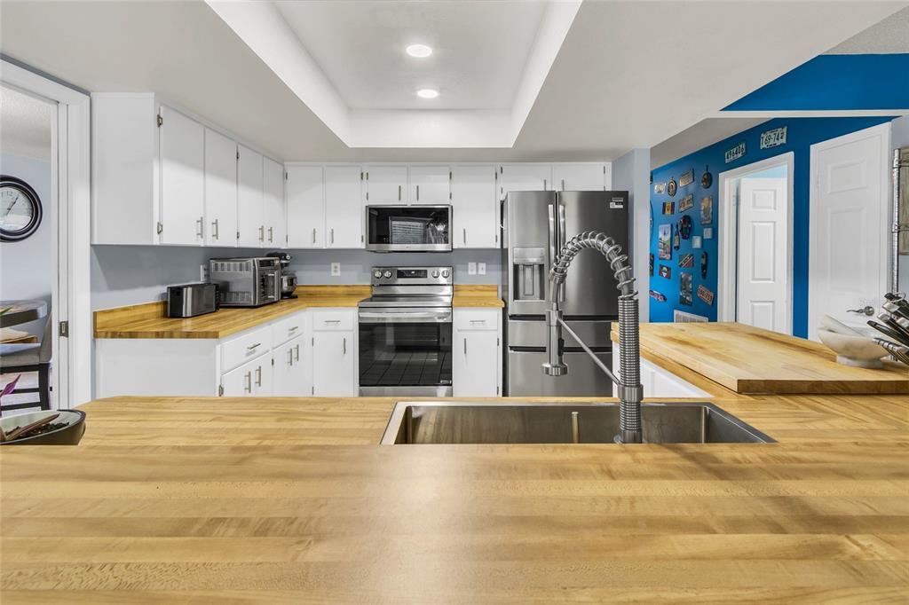 A kitchen features white cabinets, butcher block countertops, stainless steel appliances, and a blue wall — 1372 HAULOVER AVENUE, SPRING HILL, FL