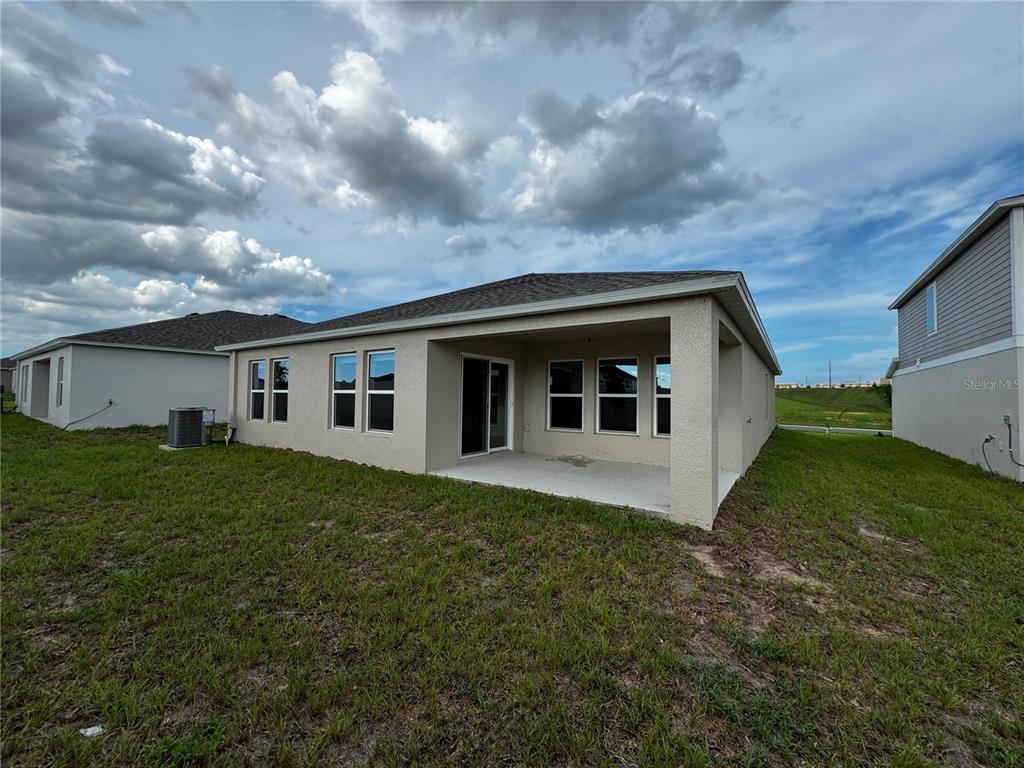 The exterior rear view of a house features a covered patio and a grassy yard — 1338 PALMEROY ROAD, HAINES CITY, FL