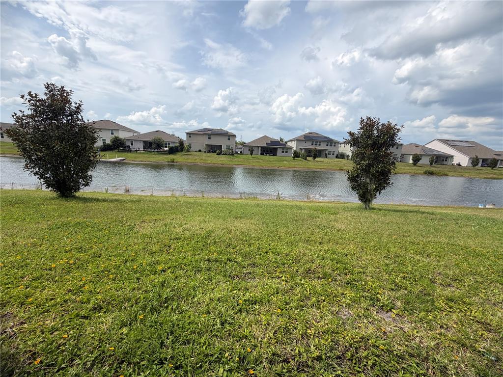 A grassy lawn overlooks a pond with several suburban houses in the background — 4921 LOTTA COURT, ST CLOUD, FL