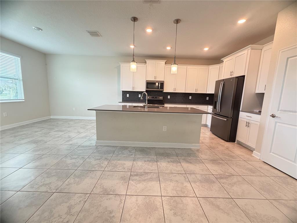 A kitchen features white cabinets, a dark island, stainless appliances, and light-colored tile flooring — 4921 LOTTA COURT, ST CLOUD, FL