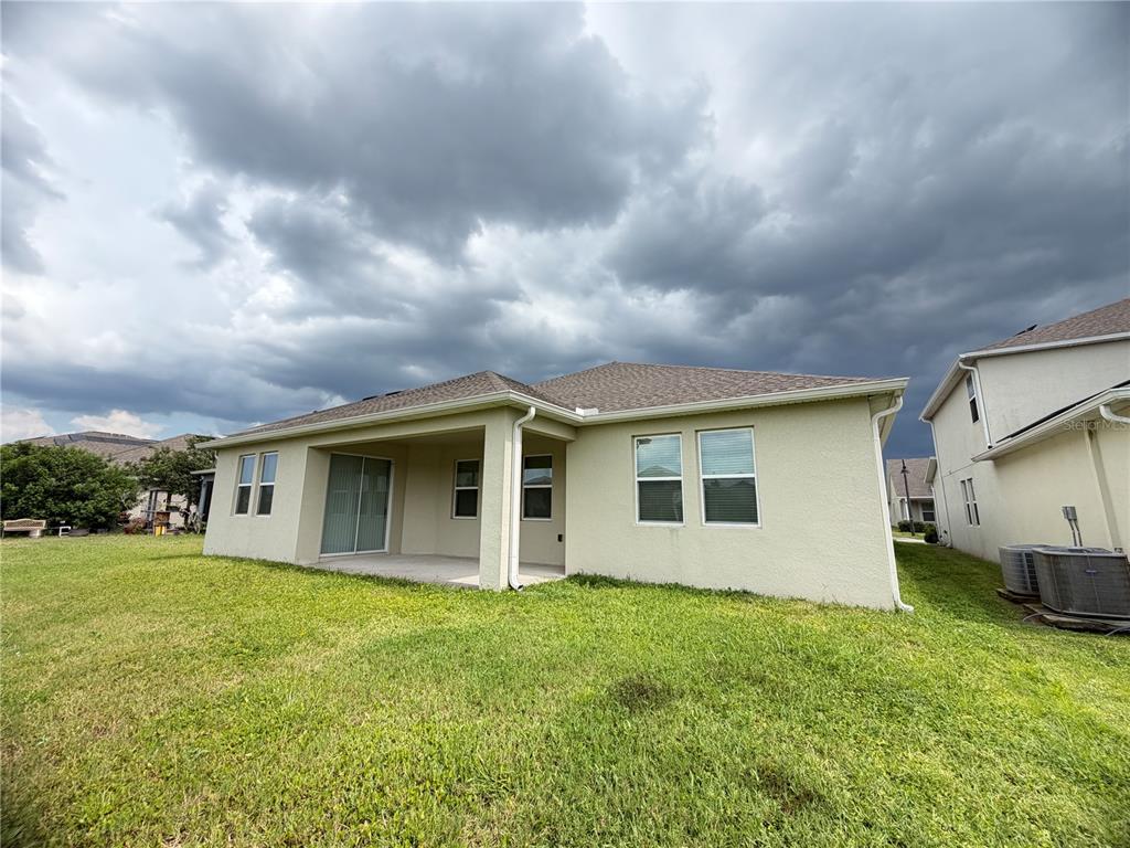 The exterior rear view of a single-story house features a covered patio and a lawn — 4921 LOTTA COURT, ST CLOUD, FL
