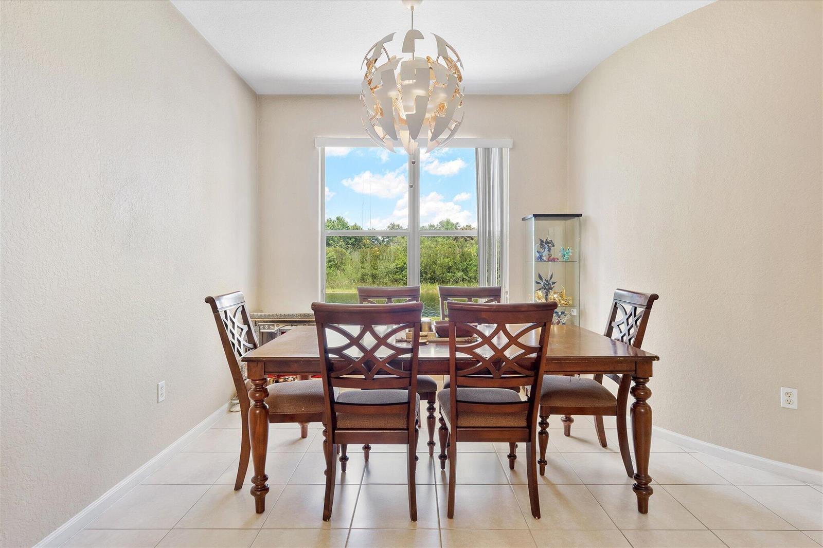 A dining room features a wooden table with six chairs, a modern chandelier, and a window — 16385 SW 27th Street, Miramar FL 33027, MIRAMAR, FL