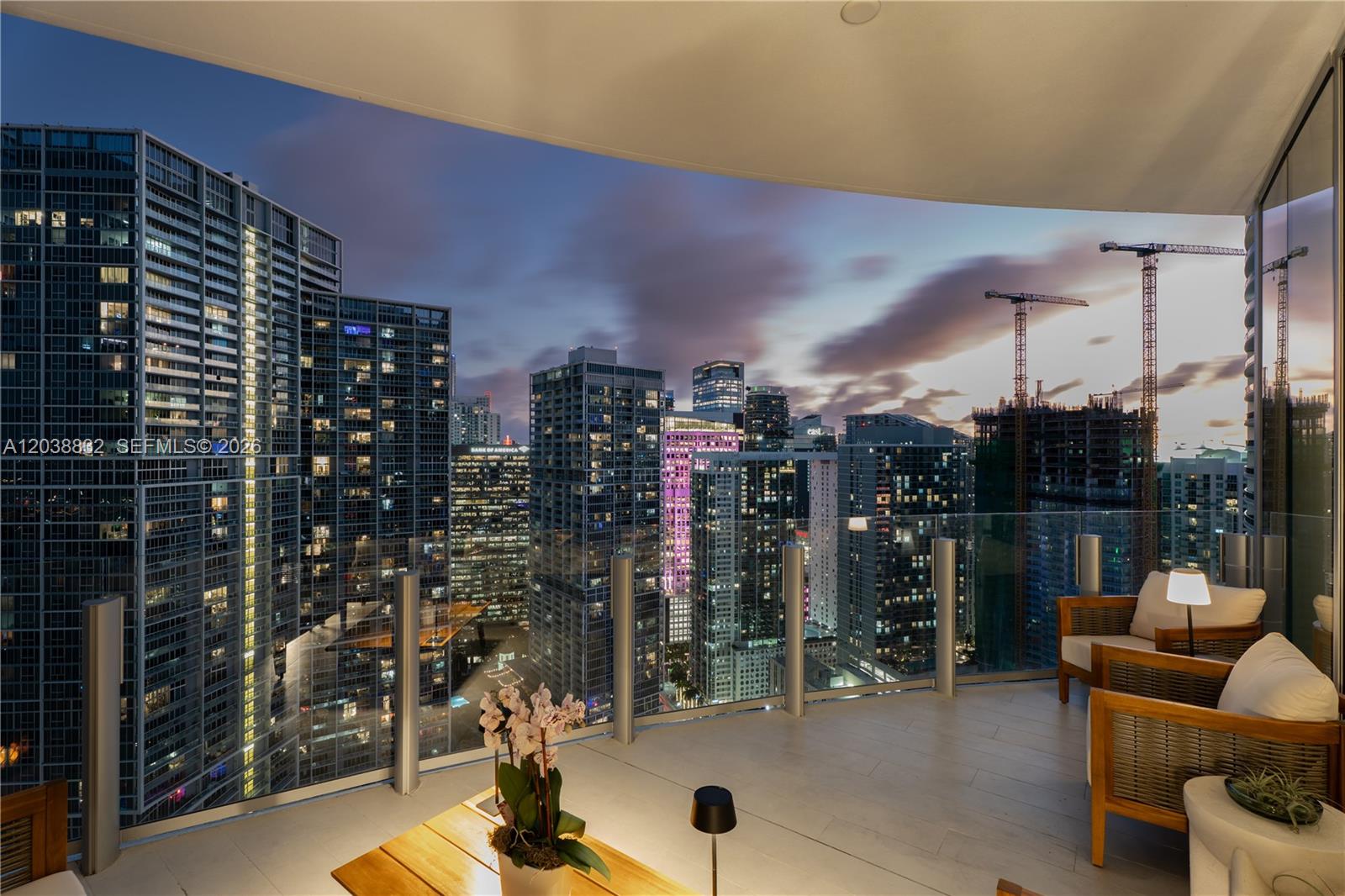 A high-rise balcony with outdoor seating overlooks a dense city skyline at dusk — 300 Biscayne Boulevard Way # 4007W, Miami FL 33131, MIAMI, FL