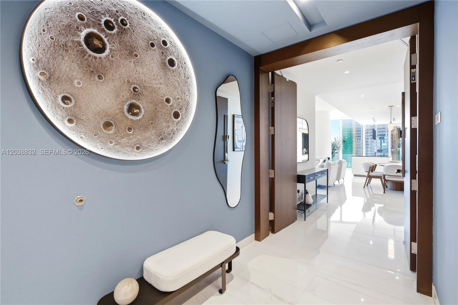 A blue-walled entryway features a large circular moon art piece, a mirror, and a bench — 300 Biscayne Boulevard Way # 4007W, Miami FL 33131, MIAMI, FL