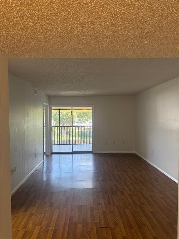 An empty living room with wood-look flooring, a popcorn ceiling, and a sliding glass door — 861 SKY LAKE CIRCLE UNIT C, ORLANDO, FL