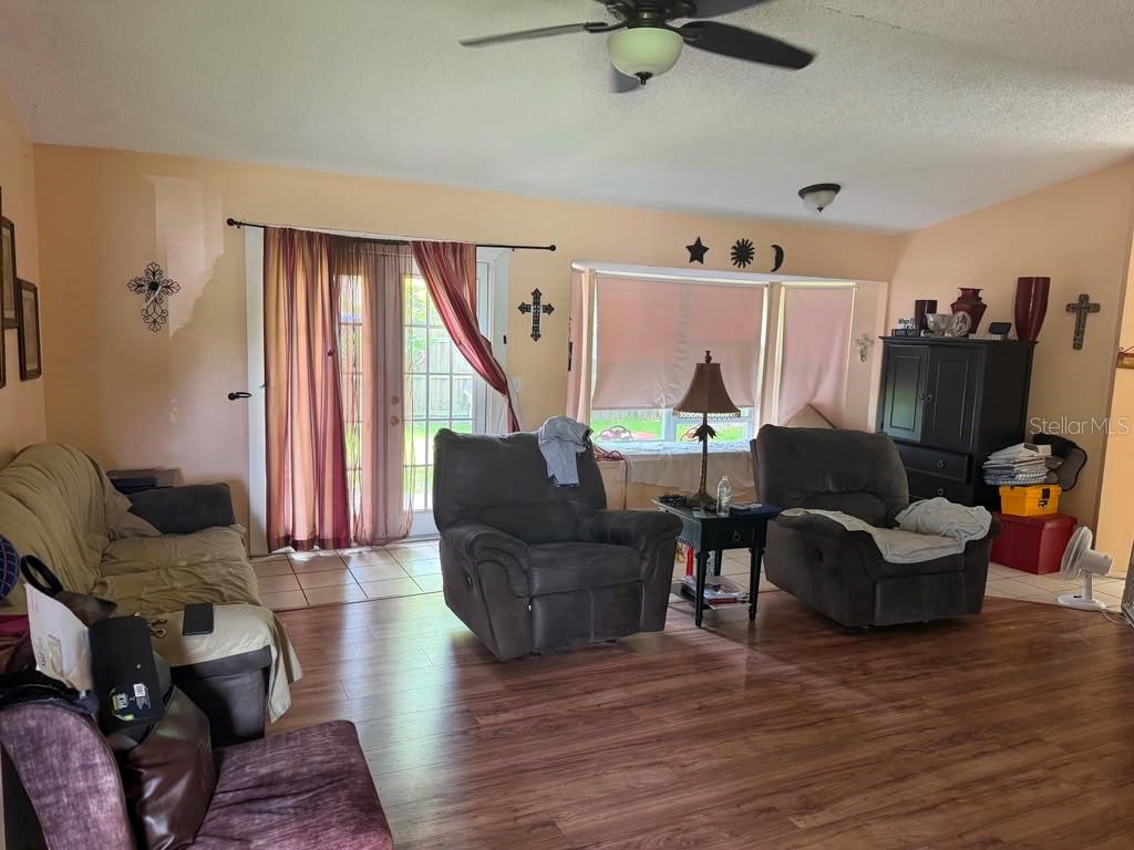 A living room features wood-look flooring, two gray recliners, a sofa, and sliding glass doors — 2114 WIND JAMMER COURT, KISSIMMEE, FL