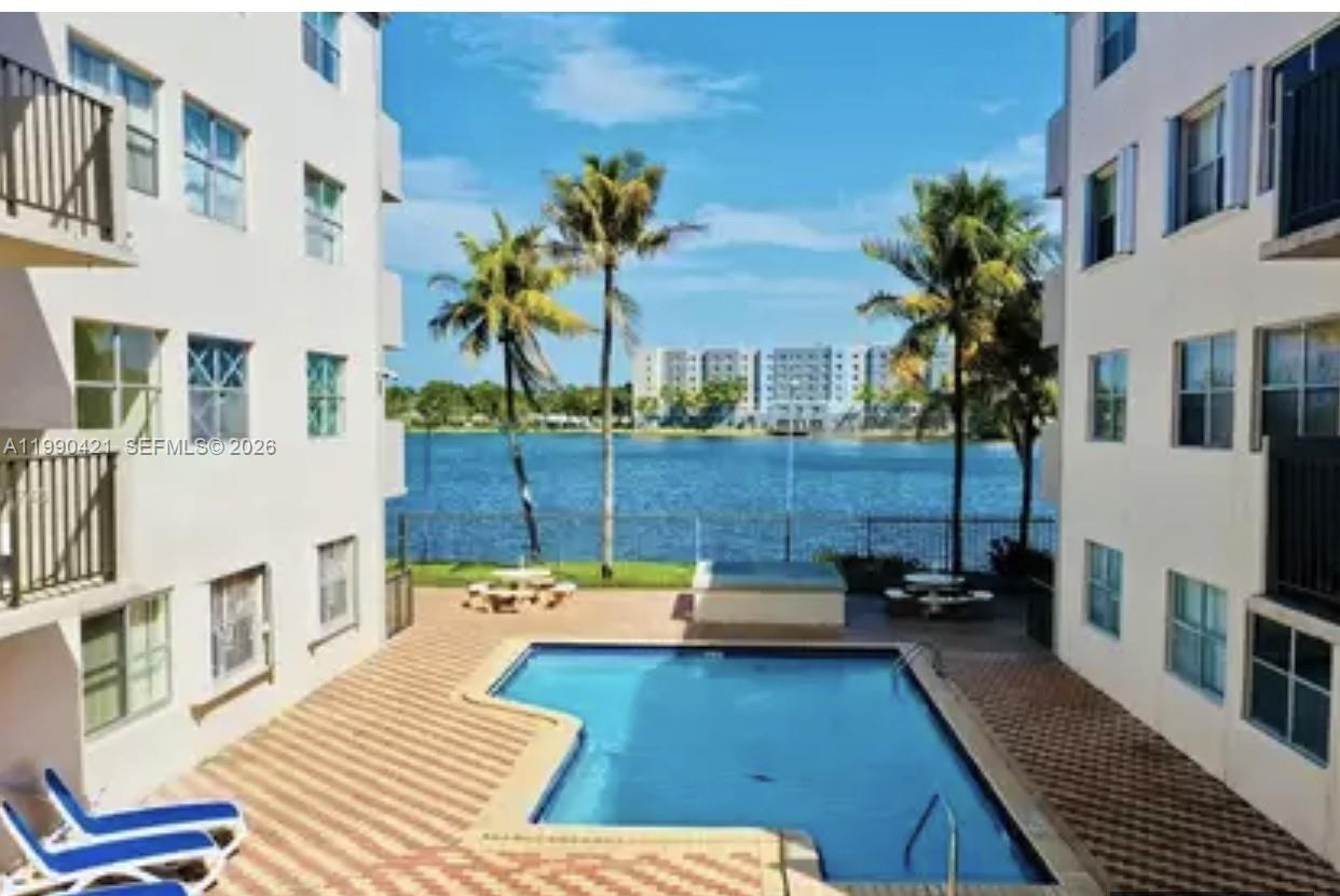 A swimming pool sits between two apartment buildings overlooking a lake with palm trees — 5501 NW 7th St # E219, Miami FL 33126, MIAMI, FL